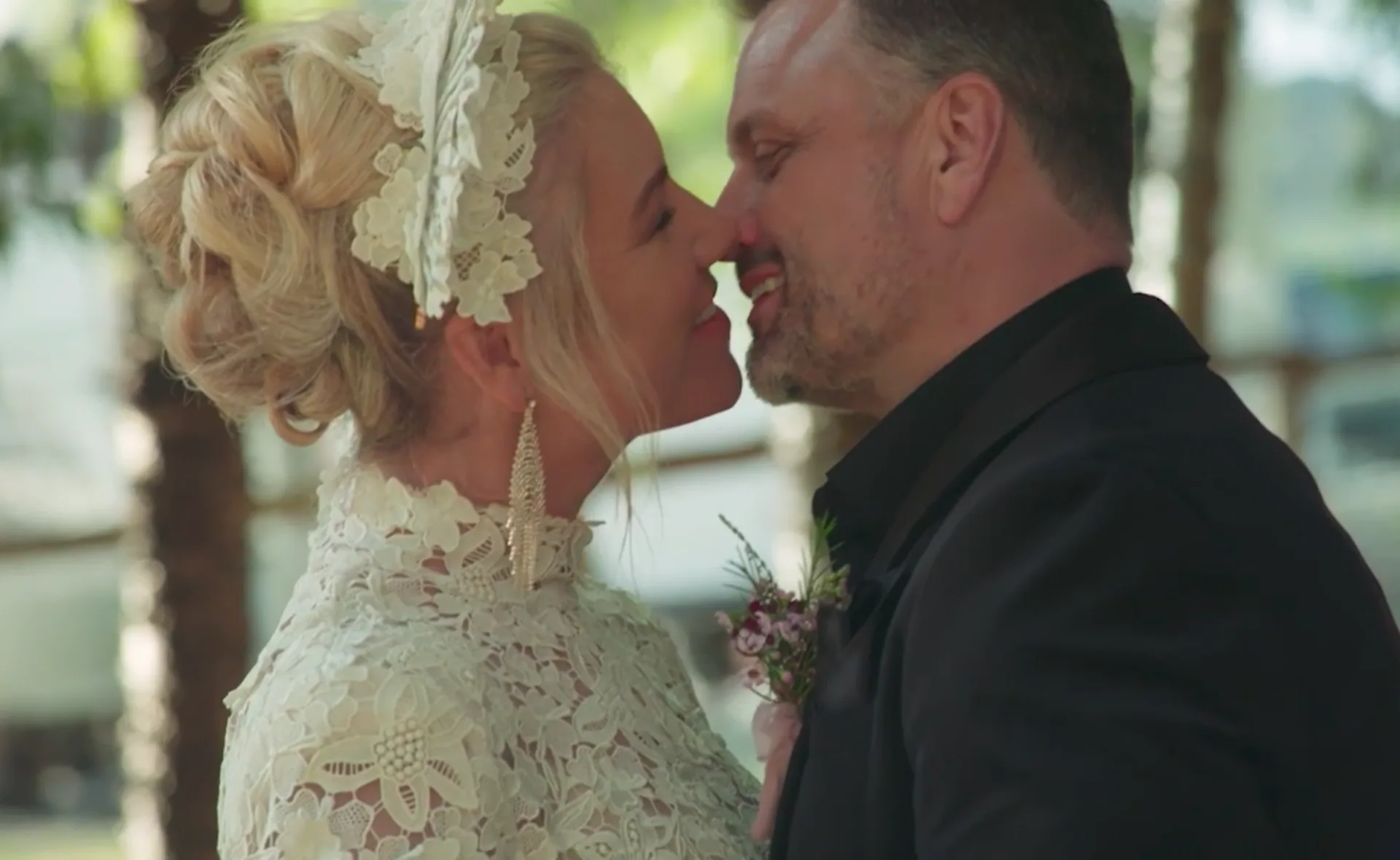 A couple smiling and touching noses, dressed in wedding attire.
