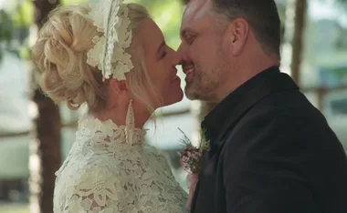 A couple smiling and touching noses, dressed in wedding attire.