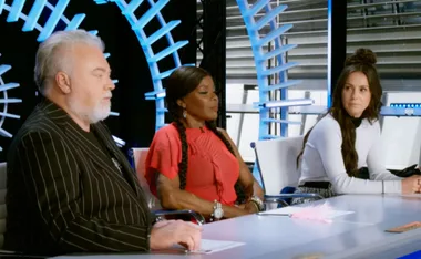 Judges sitting at a panel in a studio setting with modern, glowing design elements in the background.
