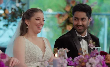 A smiling bride and groom sitting at a decorated table during their wedding reception.