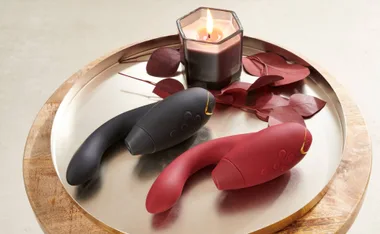 Black and red vibrators on a tray with a lit candle and decorative leaves beside them.