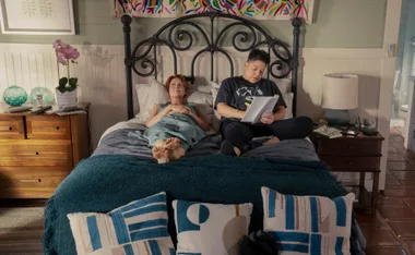 Two people relaxing on a bed, one reading, in a cozy, colorful bedroom setting.