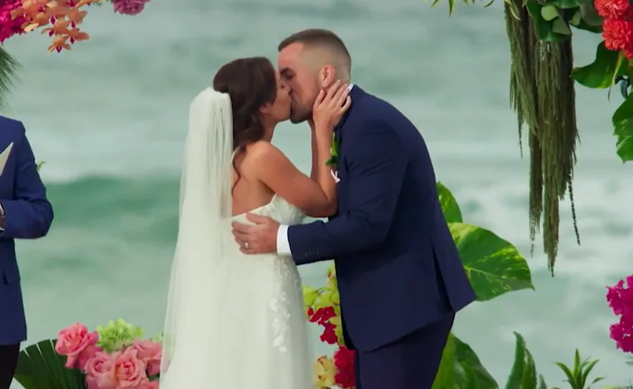 Bride and groom kiss at a beach wedding altar adorned with colorful flowers.