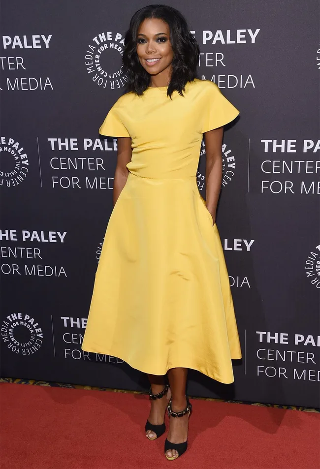 A woman in a yellow dress poses on the red carpet at The Paley Center for Media event.