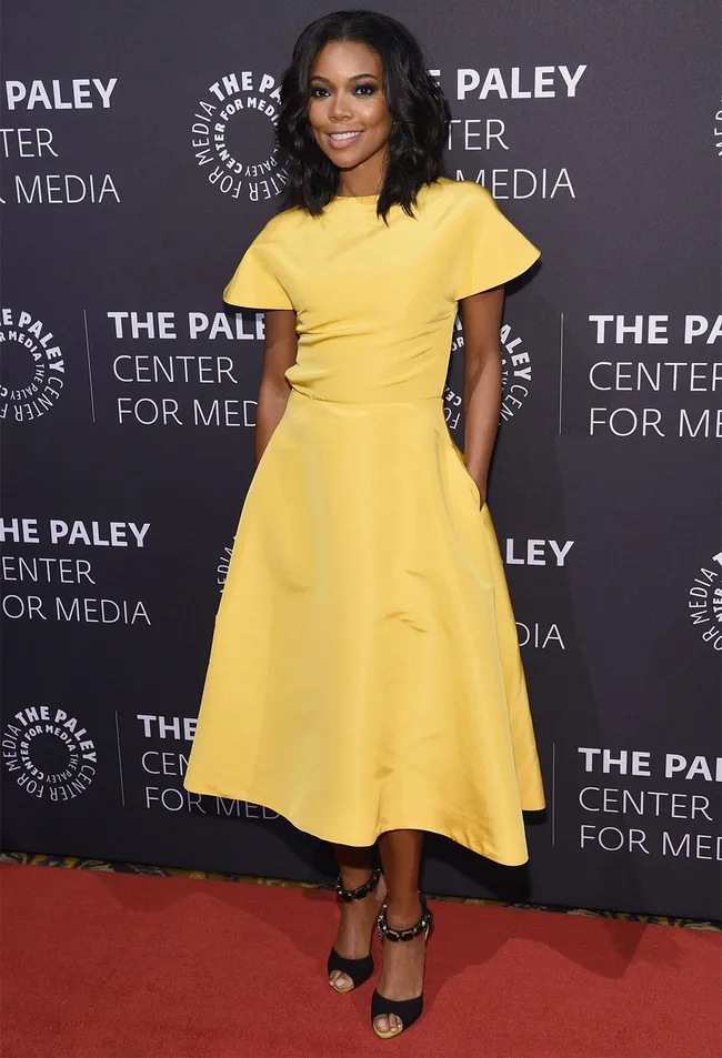 A woman in a yellow dress poses on the red carpet at The Paley Center for Media event.