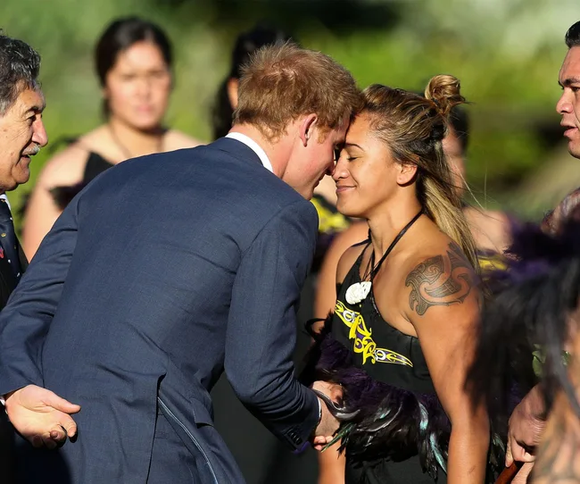 A man in a suit and a woman in traditional attire exchange a Maori hongi greeting, touching noses.
