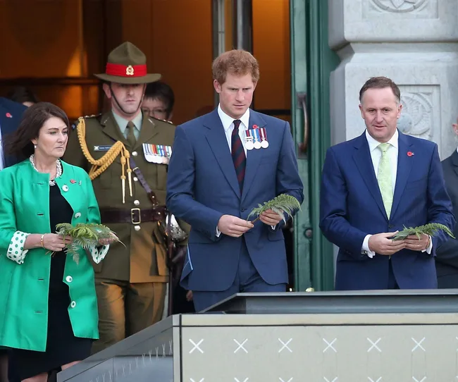 Three people holding ferns while standing outside a building, with a soldier in uniform behind them.