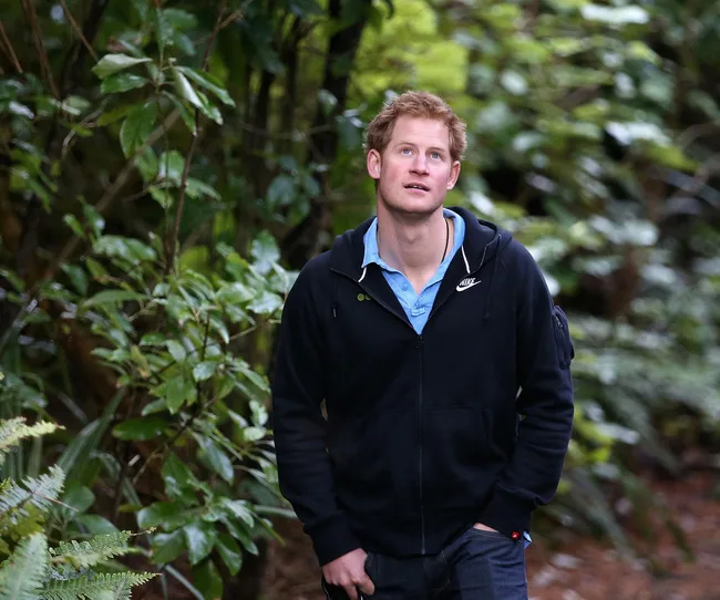 Young man with red hair in a black hoodie walking through a forest, looking upwards thoughtfully.