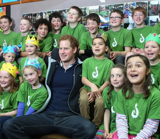 A man with children in green shirts with crowns, smiling and posing for a group photo indoors.