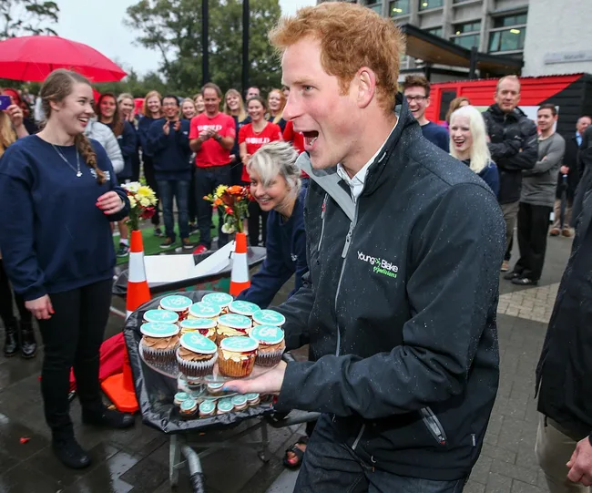 Man holding cupcakes while people around him smile and clap in an outdoor gathering.
