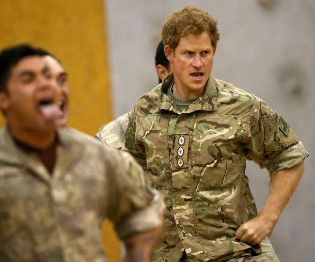 A person in military uniform with others, appearing to perform a haka dance, expressing intensity and focus.