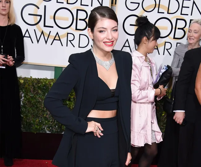 Person in a stylish black outfit with a necklace at a red carpet event.