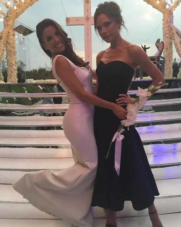 Two women posing elegantly, one in a white gown and the other in a black dress, in a decorated outdoor setting.