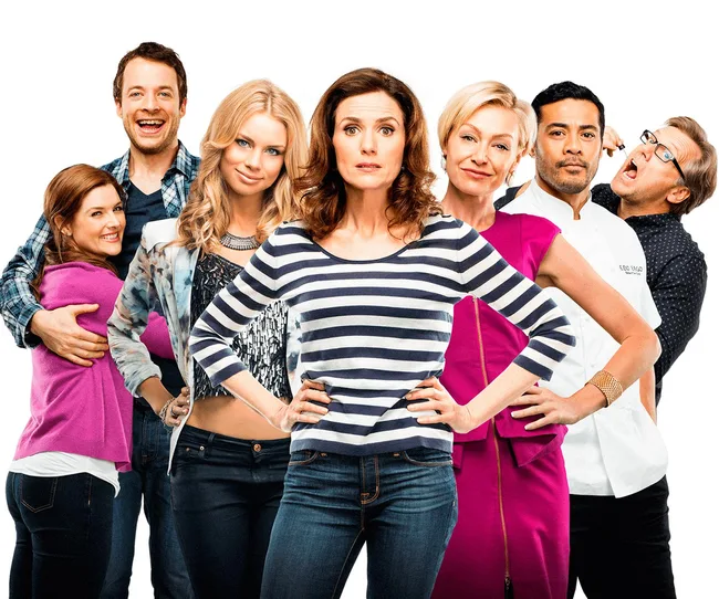 Group of seven people standing together, with the woman in stripes at the center, all wearing casual and formal attire.