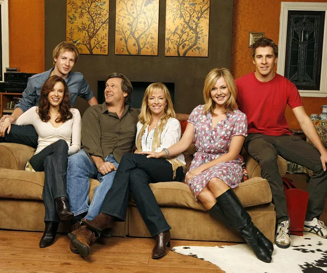 Group of six people sitting and smiling in a living room setting.