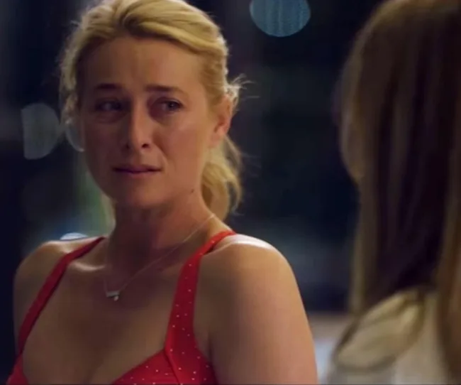A woman with blonde hair in a red dress appears emotional, standing in front of another person at night.