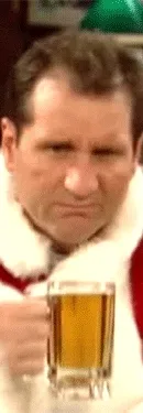 Man dressed as Santa Claus, holding a beer mug, sitting at a bar with a serious expression.