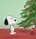 Snoopy stands surprised in front of a decorated Christmas tree with ornaments and a candy cane.
