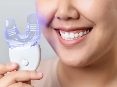 person smiling and holding a teeth whitening kit and LED light