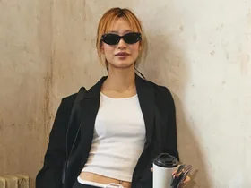 Person in black blazer with coffee cup on left; beige suits on hangers on right.