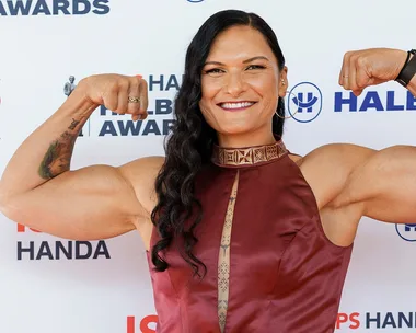 Woman in a burgundy dress flexing her arms, smiling at the Halberg Awards backdrop.