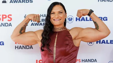 Woman in a burgundy dress flexing her arms, smiling at the Halberg Awards backdrop.