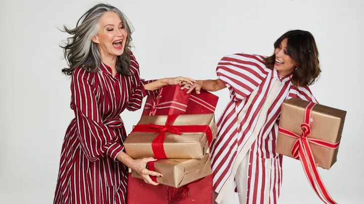 Two women in matching striped outfits joyfully holding wrapped gifts with red ribbons.