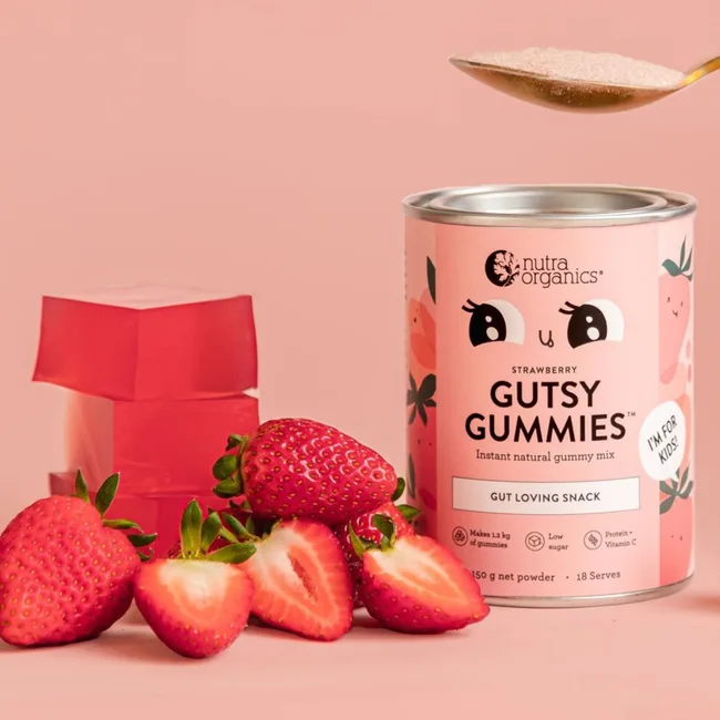Strawberry Gutsy Gummies can with fresh strawberries and gelatin blocks on a pink background.