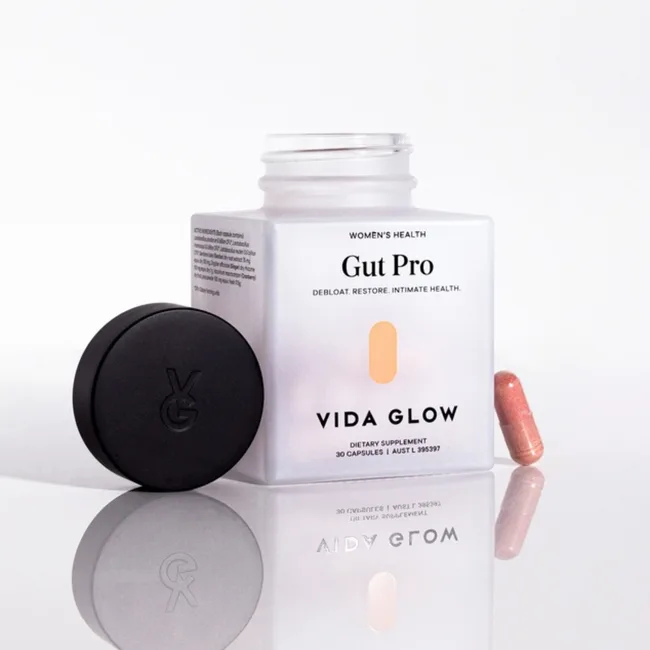Open jar of Vida Glow Gut Pro supplement with one pink capsule and black lid beside it.