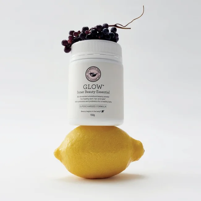 A jar of GLOW Inner Beauty Essential powder balanced on a lemon with grapes on top.