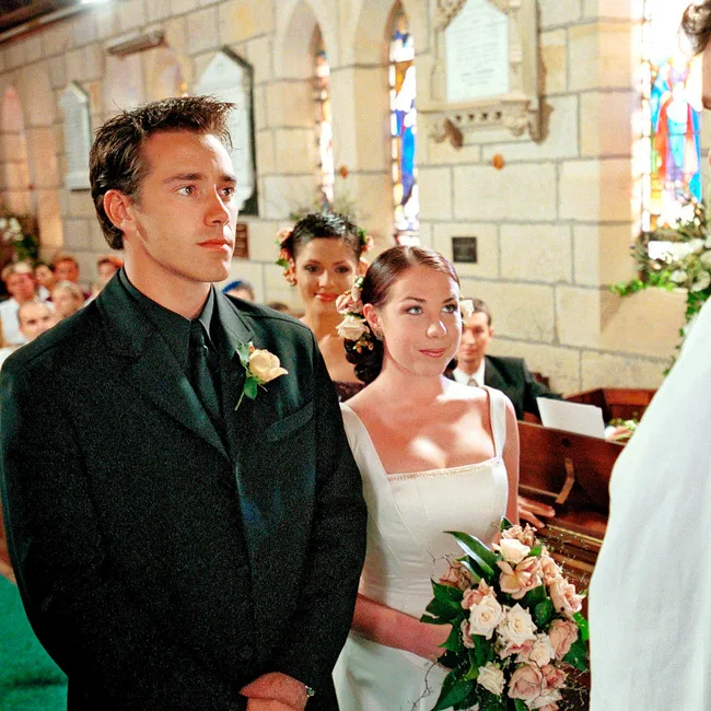 A bride and groom stand at the altar in a church, holding flowers, with guests seated in the background.