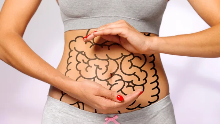 A woman in fitness attire with a digestive system illustration on her abdomen, hands framing the stomach area.