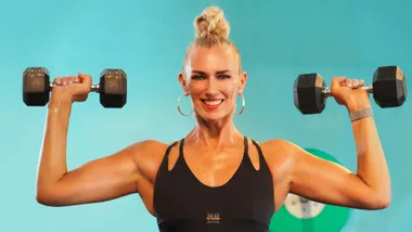 Smiling woman in black sportswear holding dumbbells against a turquoise background.