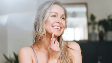 Woman smiling while using a facial tool in a bright, airy room.