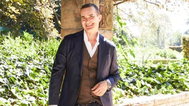John Aiken leaning against a low wall, smiling