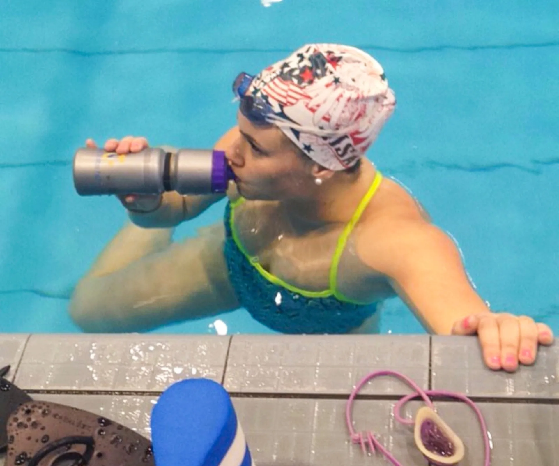 Nikki Johns at the edge of the pool drinking out of a water bottle