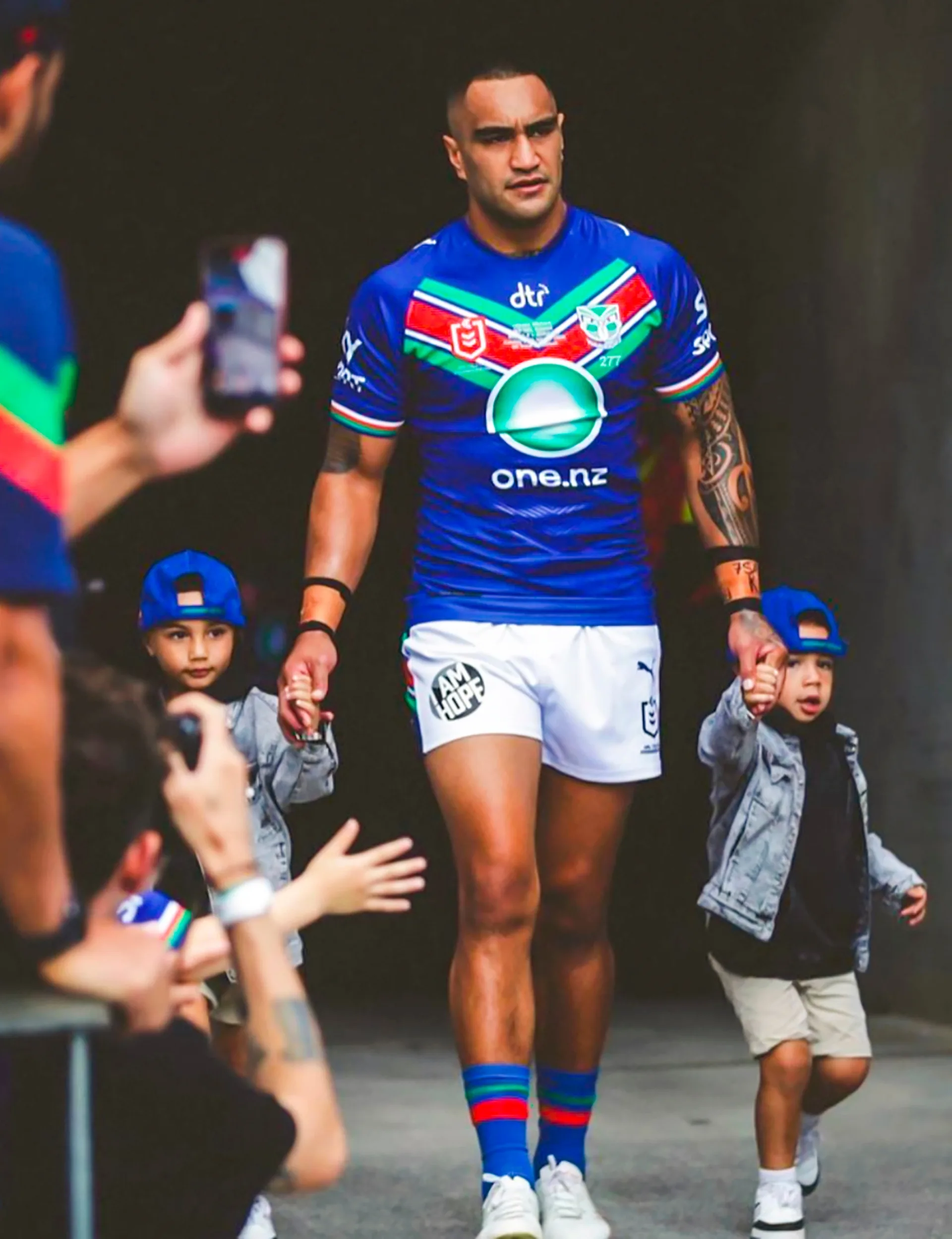 Marata Niukore walking out of the tunnel and onto the Rugby League field in his Warriors kit, holding each of his sons' hands