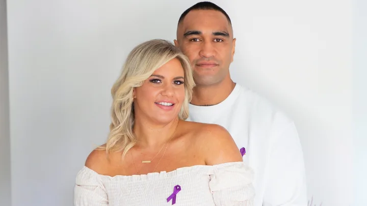 Marata Niukore with his arms around his partner, Nikki Johns, both wearing white with a purple ribbon pinned to their chests