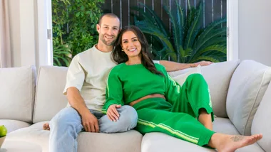 Aesha in a green tracksuit leaning on partner Scott on the couch
