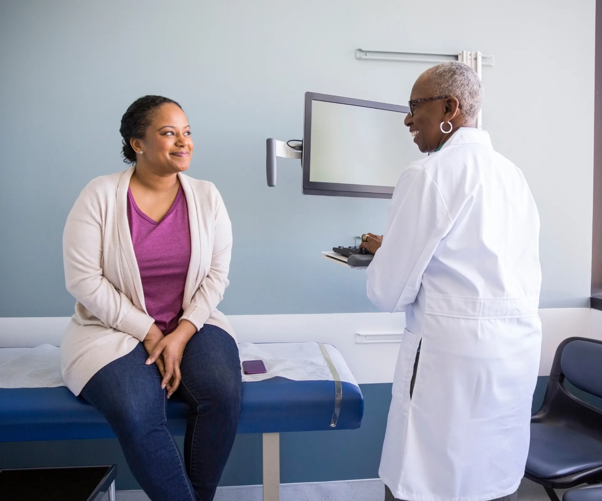 A woman sitting on a doctor's bed speaking to a doctor about her midlife health