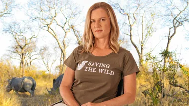 Woman in a "Saving the Wild" shirt sits outdoors with rhinos in the background.