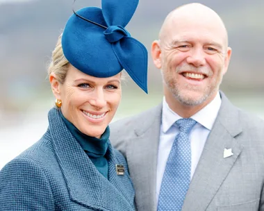 A smiling woman in a blue hat and coat stands beside a man in a gray suit and tie.