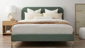 Modern bedroom with green upholstered bed, white and beige bedding, wooden nightstand, and abstract art.