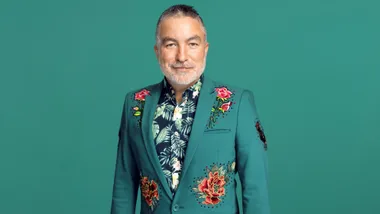 Man in a green floral suit jacket, smiling against a solid green background.