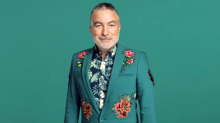 Man in a green floral suit jacket, smiling against a solid green background.