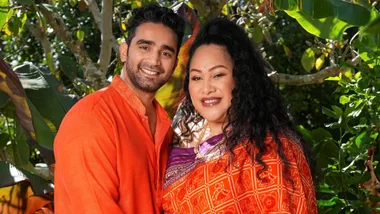 Bella and partner Suraj both wearing orange standing together in front of a bush