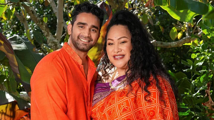 Bella and partner Suraj both wearing orange standing together in front of a bush