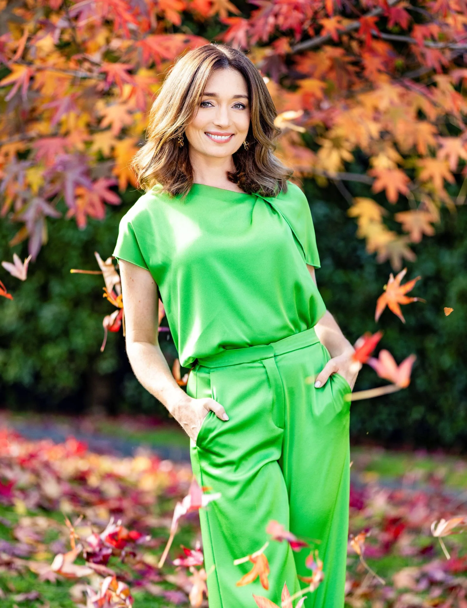 Antonia Prebble wearing a green shirt and green pants in an autumnal background, with her hands in her pockets