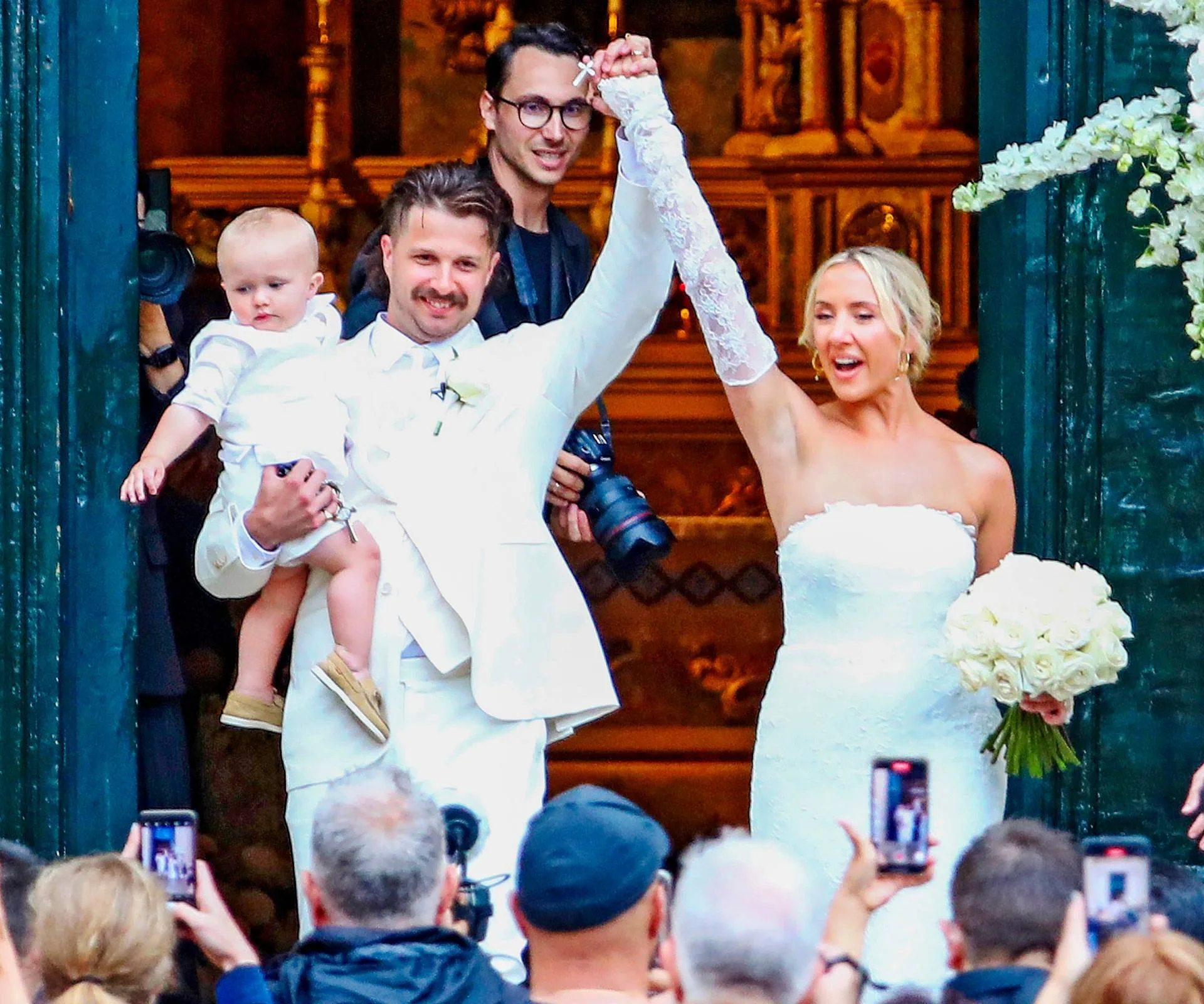 Newlyweds Liam and Nicole holding son Louie waving to a crowd of people from the venue doorway