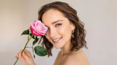 Model looking over her left shoulder at the camera and holding a rose over her right eye